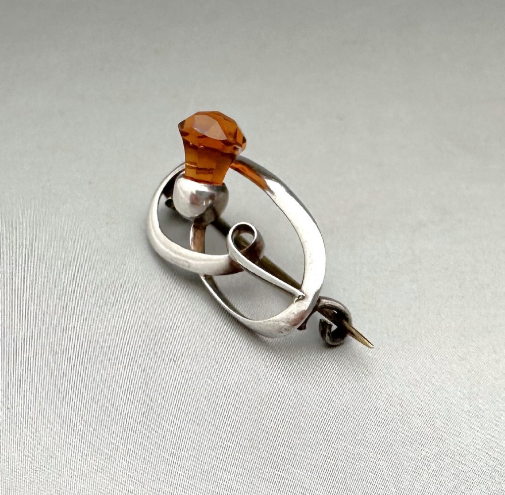 An Art Nouveau silver brooch featuring a stylised oval frame with a central thistle motif topped with a faceted amber-coloured glass stone. View III