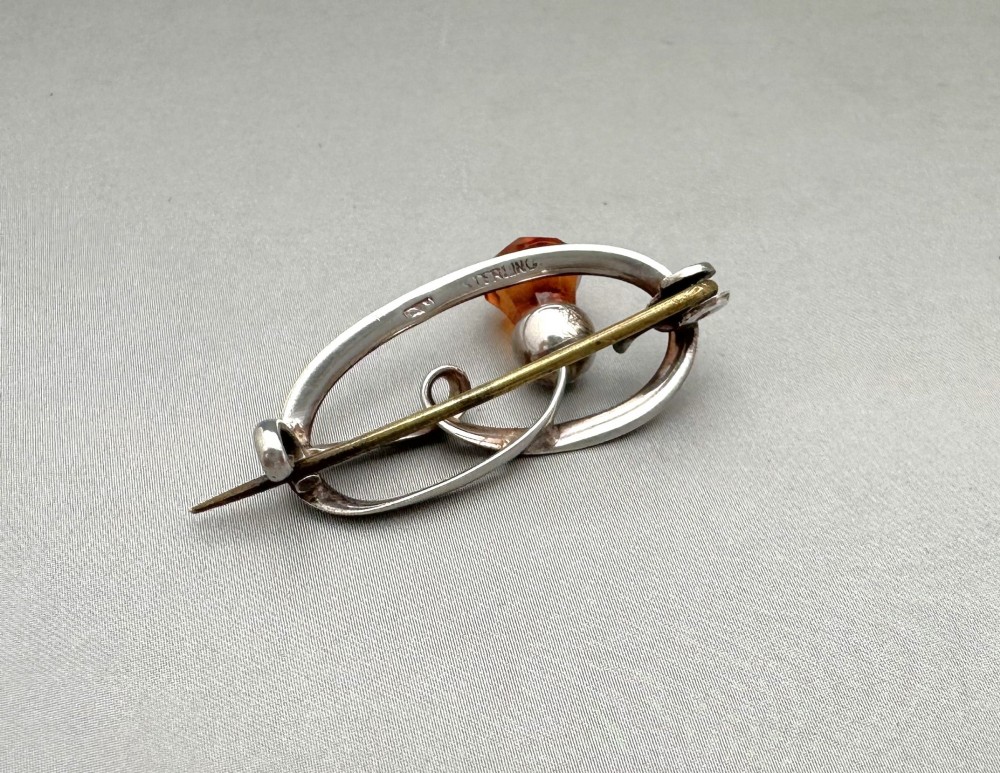 An Art Nouveau silver brooch featuring a stylised oval frame with a central thistle motif topped with a faceted amber-coloured glass stone. View IV