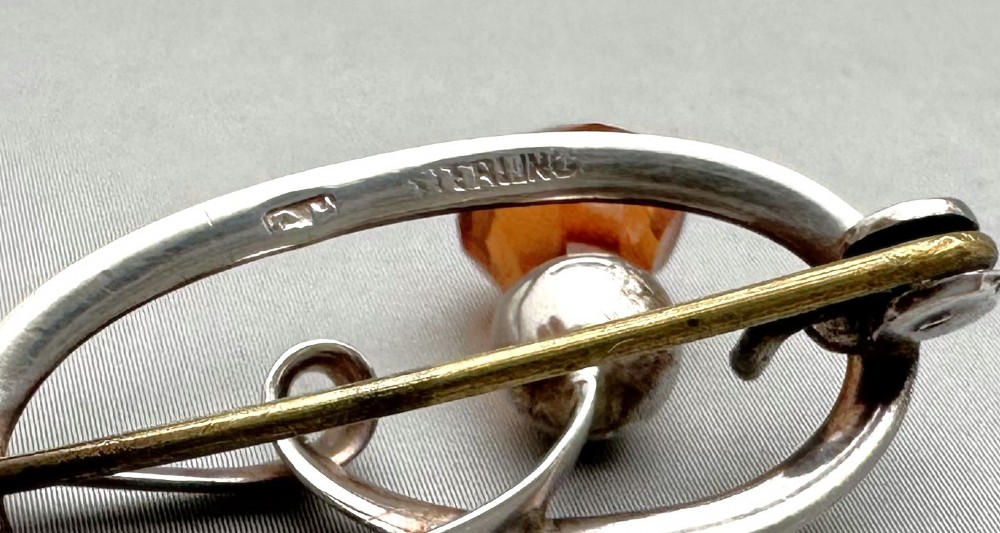 An Art Nouveau silver brooch featuring a stylised oval frame with a central thistle motif topped with a faceted amber-coloured glass stone. View V
