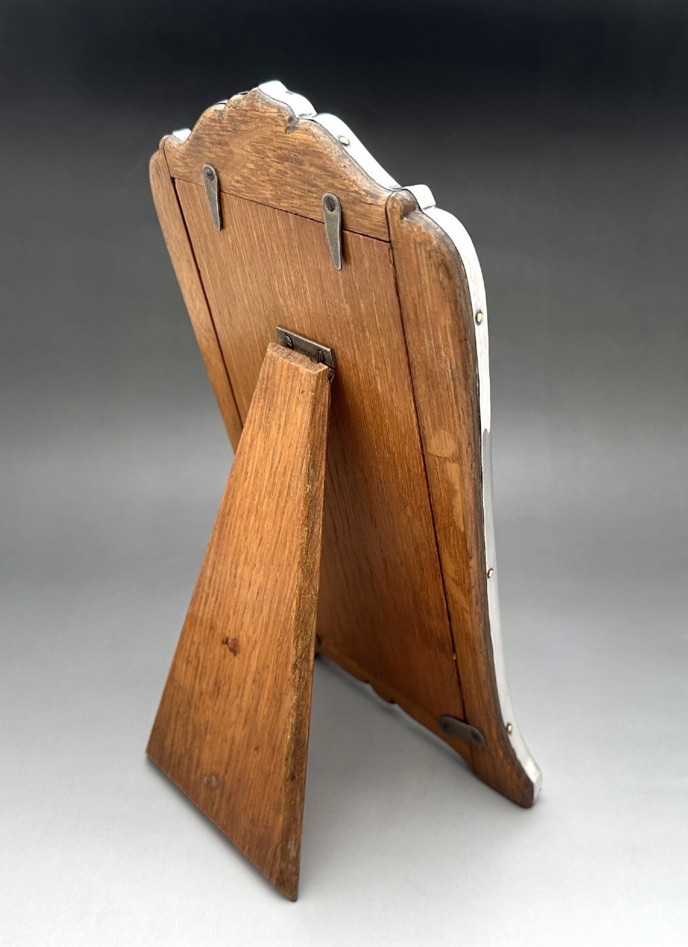 A George V polished silver picture frame with a shaped arched top and a dark wooden easel backing. View IV