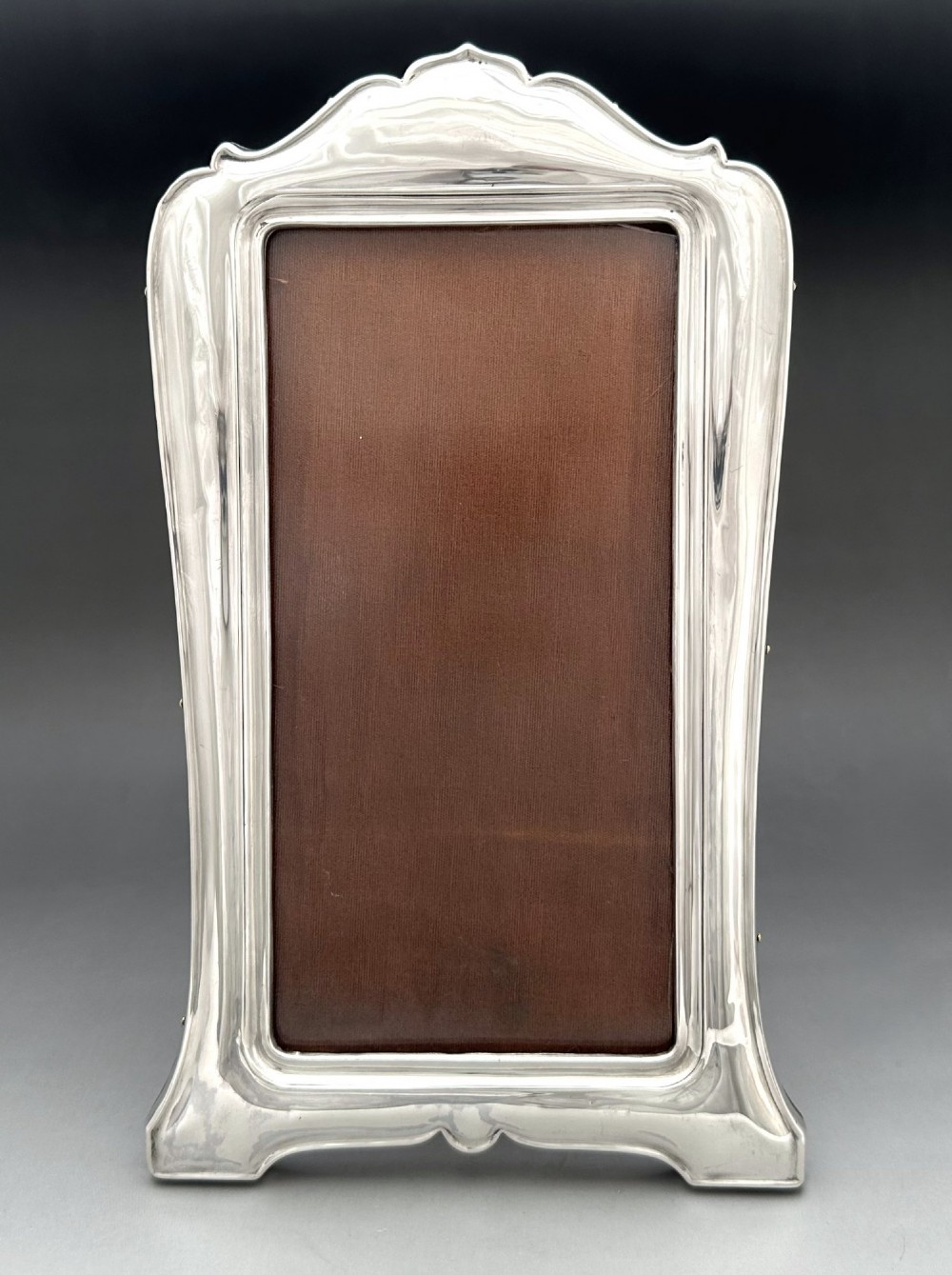 A George V polished silver picture frame with a shaped arched top and a dark wooden easel backing. View V