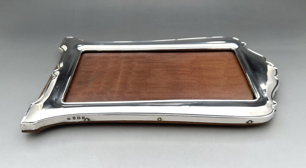 A George V polished silver picture frame with a shaped arched top and a dark wooden easel backing. View VI