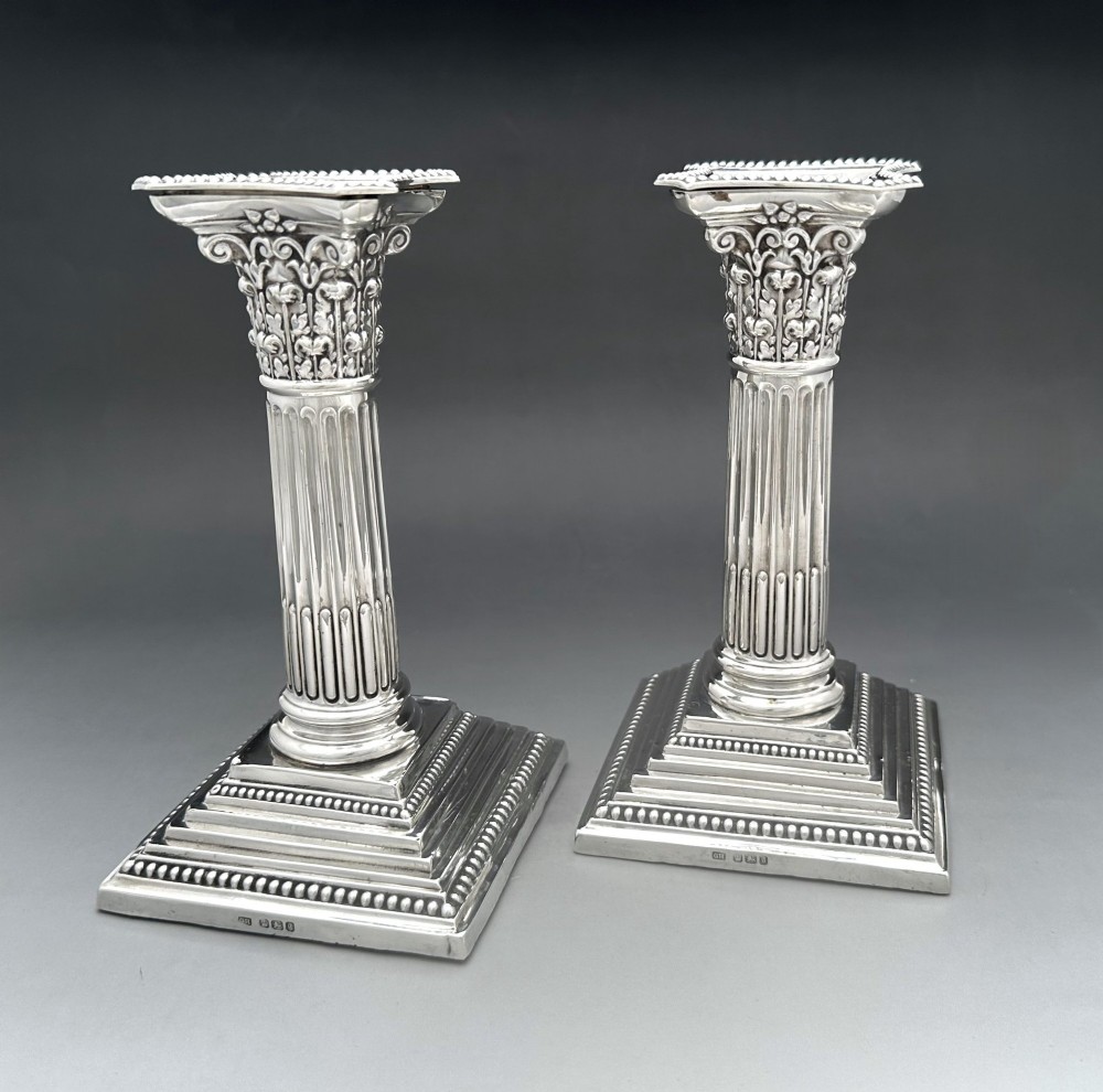A pair of Victorian silver candlesticks featuring fluted Corinthian columns with acanthus leaf capitals on stepped square bases with beaded rims.
