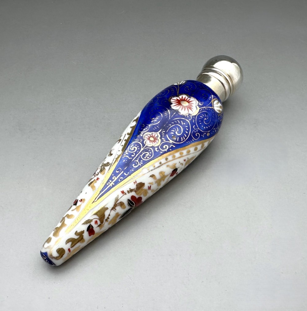A Victorian teardrop-shaped porcelain scent bottle decorated with blue, red, and gold Imari motifs, featuring a silver spherical cap.