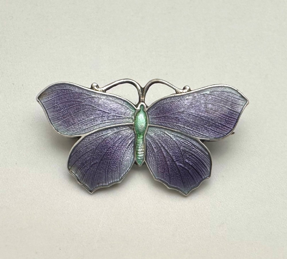 An Edwardian silver butterfly brooch featuring purple textured guilloche enamel wings and a green enamelled body.