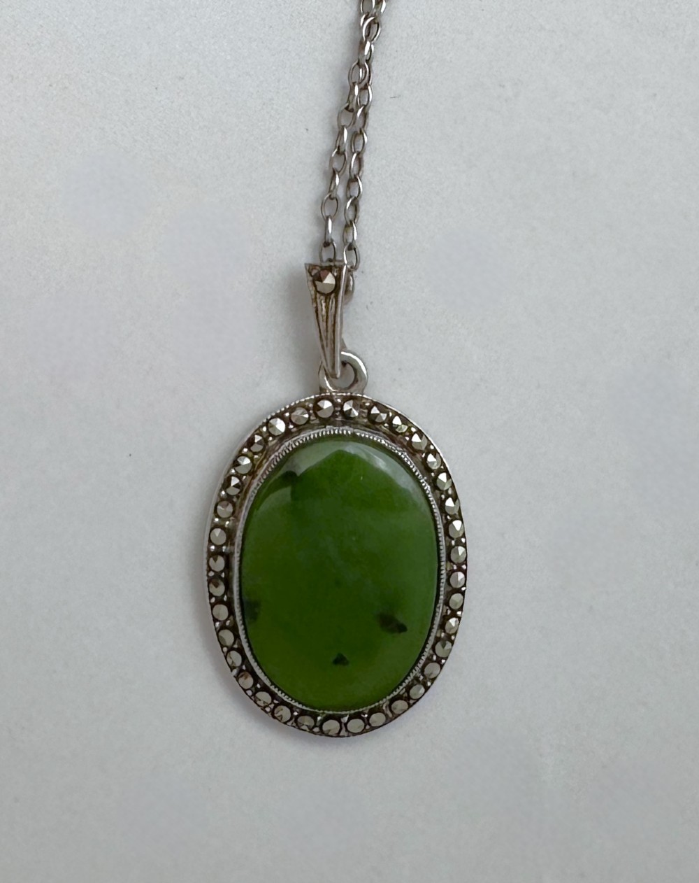An oval green jade cabochon pendant set in a decorative silver border on a fine silver link chain. View III