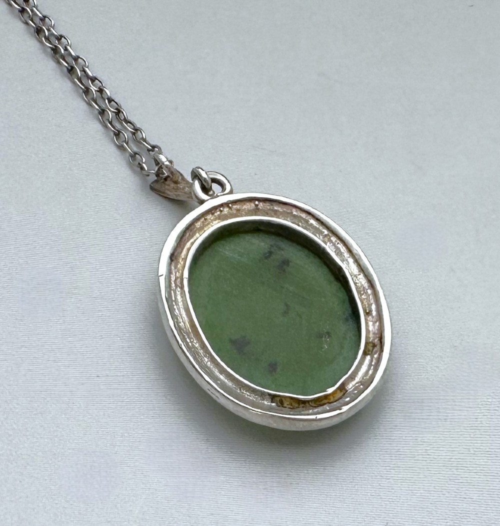 An oval green jade cabochon pendant set in a decorative silver border on a fine silver link chain. View IV