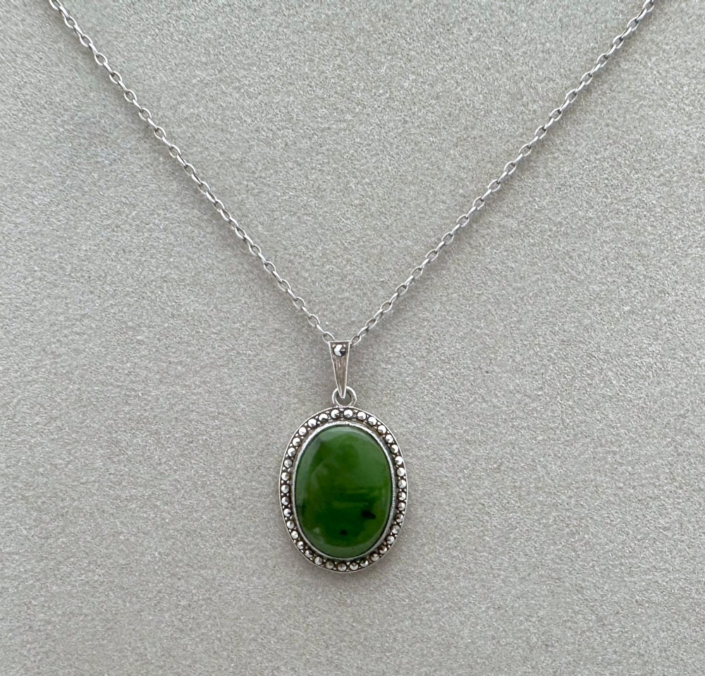 An oval green jade cabochon pendant set in a decorative silver border on a fine silver link chain.
