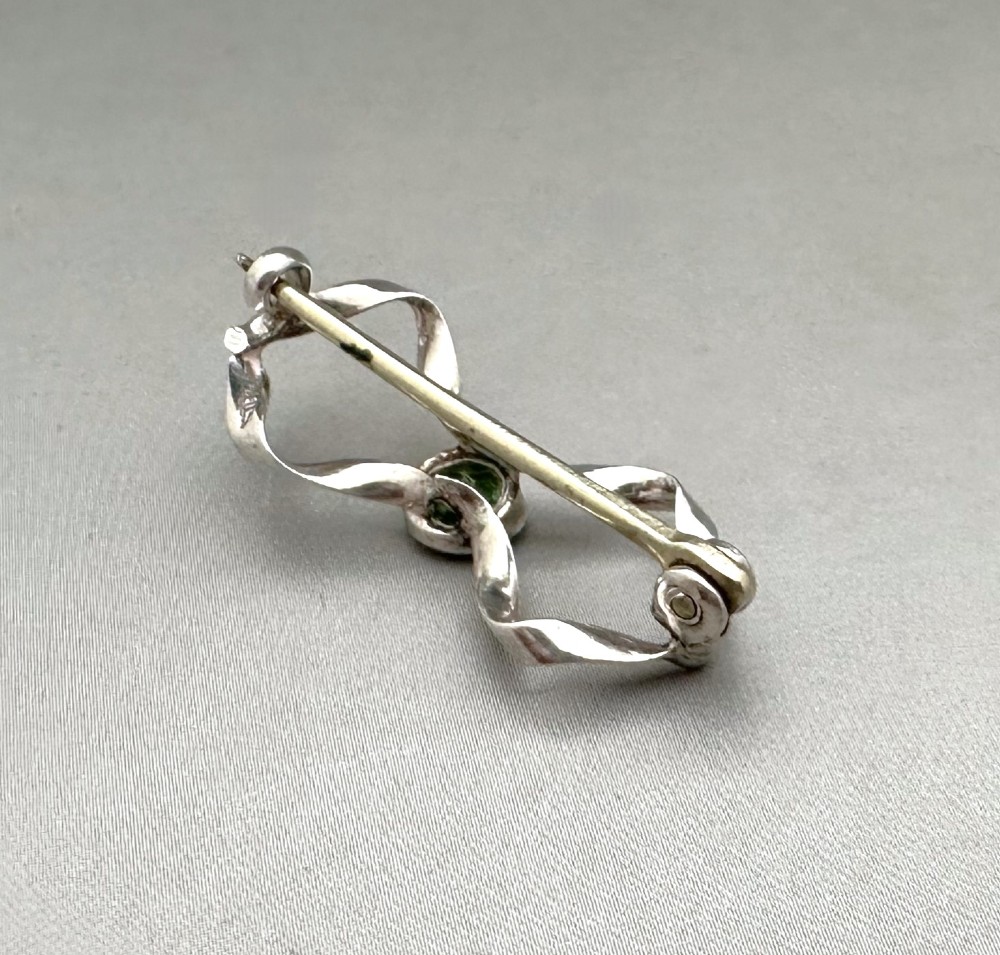 An Edwardian sterling silver brooch styled as a ribbon bow with a faceted green peridot stone set in the centre. View II