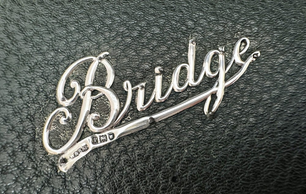 A dark green pebbled leather rectangular bridge box featuring applied silver script spelling Bridge on the top cover and a silver clasp closure. View X