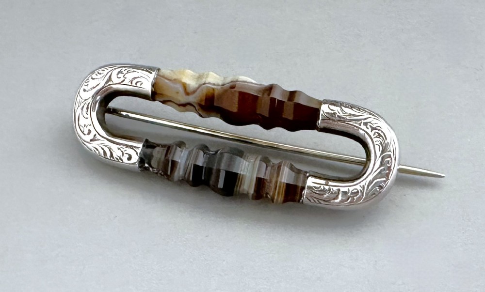 An elongated Victorian silver brooch featuring hand-engraved end mounts and faceted banded brown agate stones.