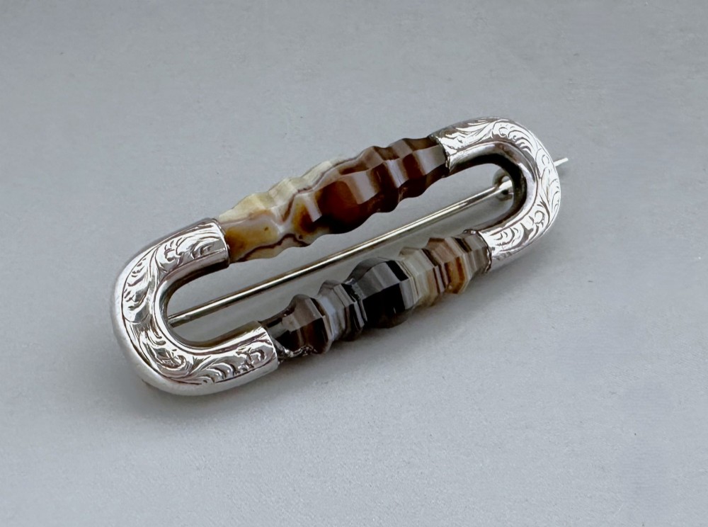 An elongated Victorian silver brooch featuring hand-engraved end mounts and faceted banded brown agate stones. View II