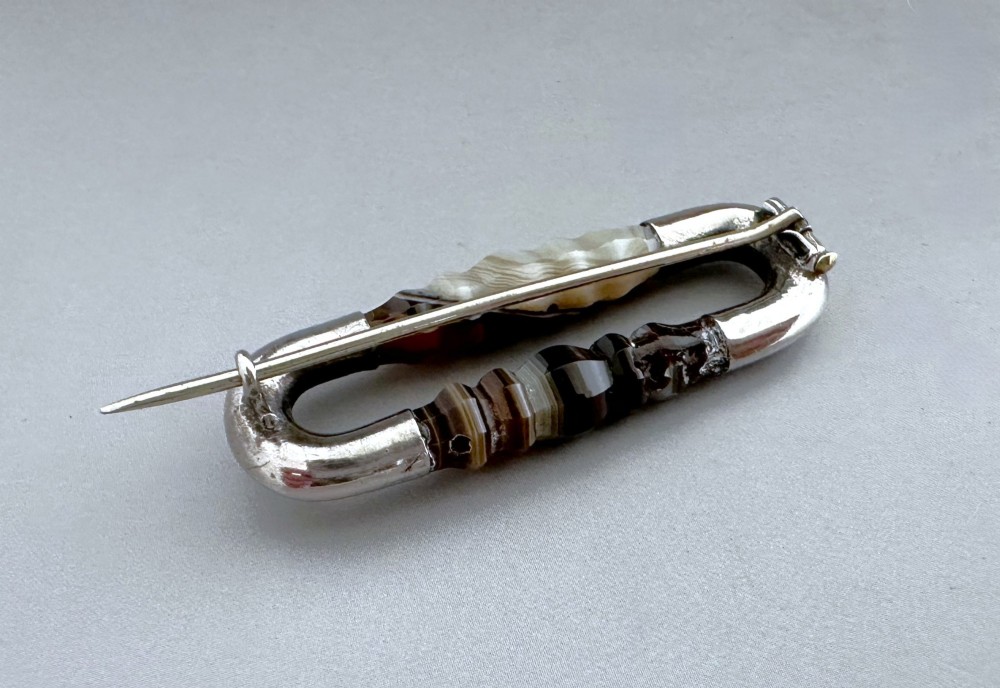 An elongated Victorian silver brooch featuring hand-engraved end mounts and faceted banded brown agate stones. View III