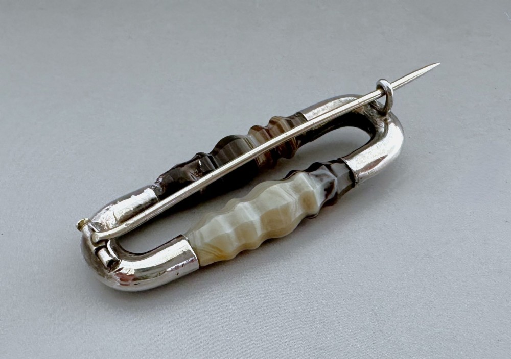 An elongated Victorian silver brooch featuring hand-engraved end mounts and faceted banded brown agate stones. View IV