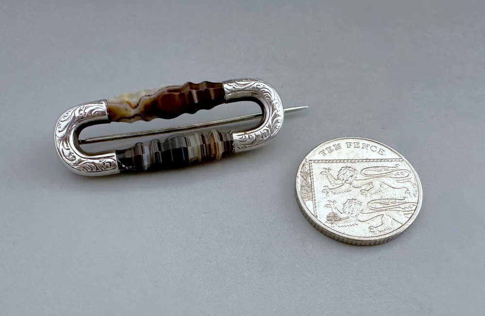 An elongated Victorian silver brooch featuring hand-engraved end mounts and faceted banded brown agate stones. View VI