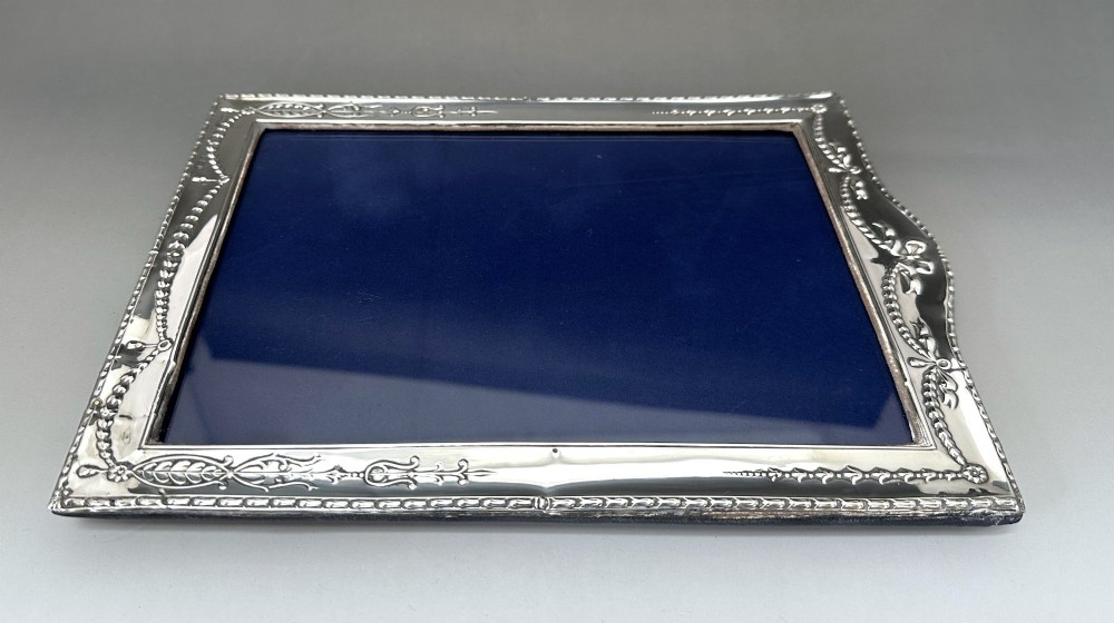 An Edwardian sterling silver portrait photo frame featuring embossed ribbon, garland, and swag decorative motifs with an arched top. View V