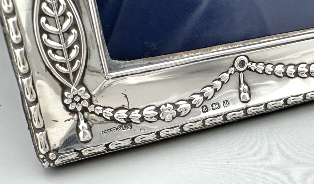 An Edwardian sterling silver portrait photo frame featuring embossed ribbon, garland, and swag decorative motifs with an arched top. View VI