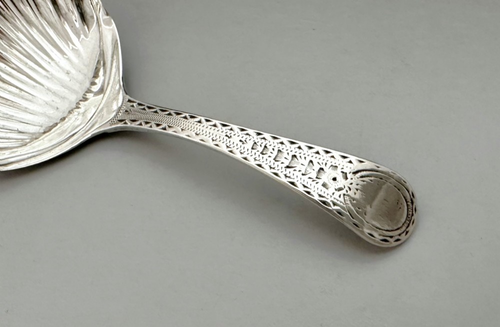 An 18th-century sterling silver caddy spoon featuring a fluted shell-shaped bowl and an intricately engraved handle. View V