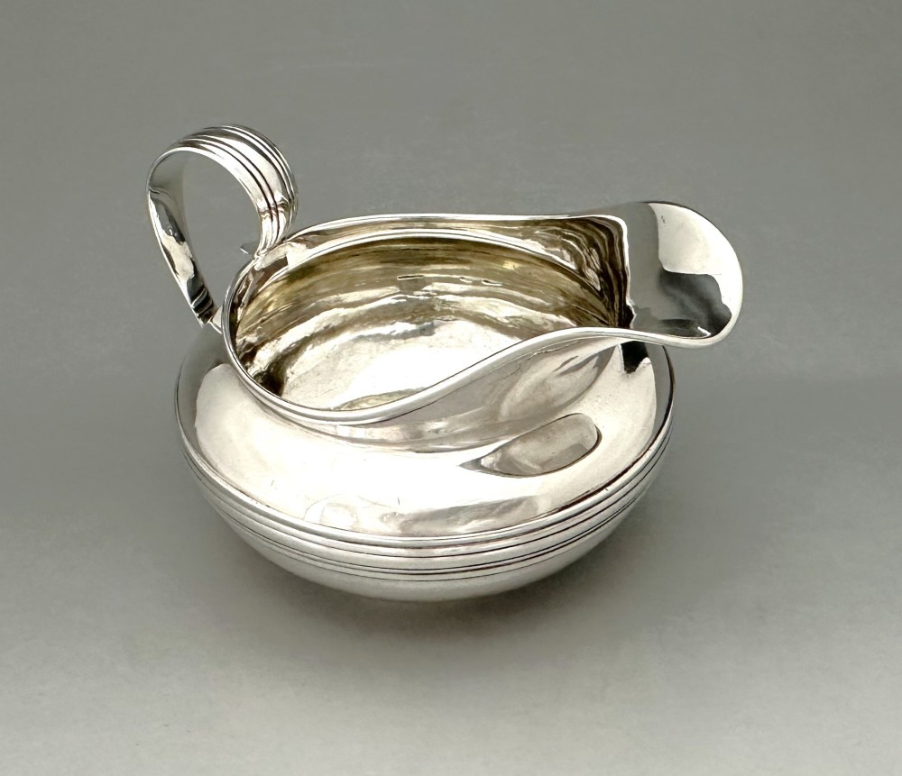 A George IV sterling silver cream jug with a polished surface, horizontal reeded decoration on the waist, a wide pour spout, and a curved high-loop handle. View III