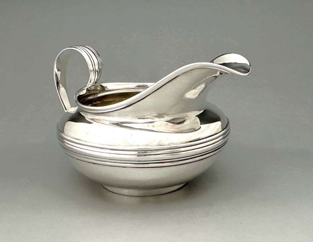 A George IV sterling silver cream jug with a polished surface, horizontal reeded decoration on the waist, a wide pour spout, and a curved high-loop handle. View IV