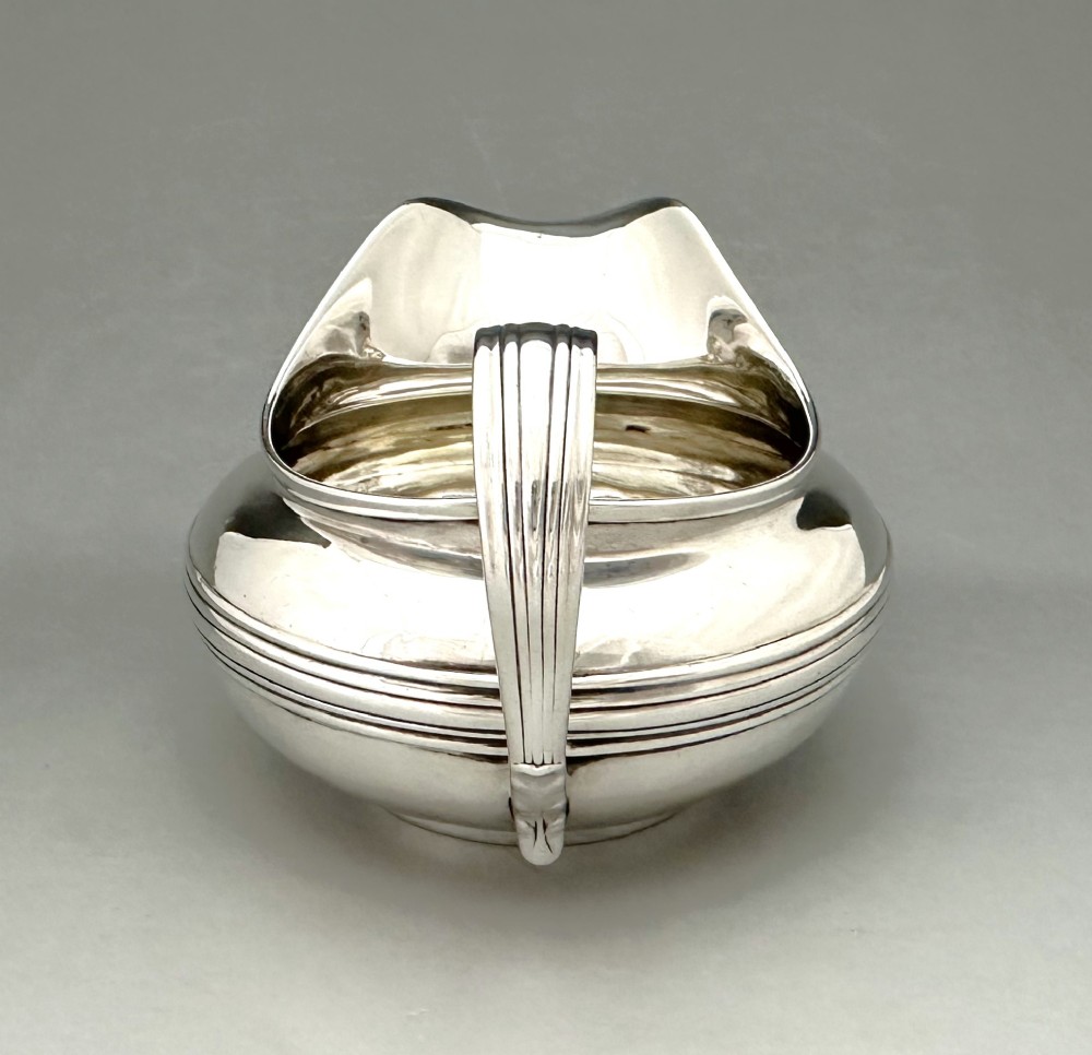 A George IV sterling silver cream jug with a polished surface, horizontal reeded decoration on the waist, a wide pour spout, and a curved high-loop handle. View V