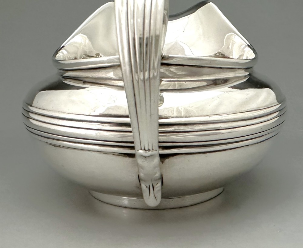 A George IV sterling silver cream jug with a polished surface, horizontal reeded decoration on the waist, a wide pour spout, and a curved high-loop handle. View VI