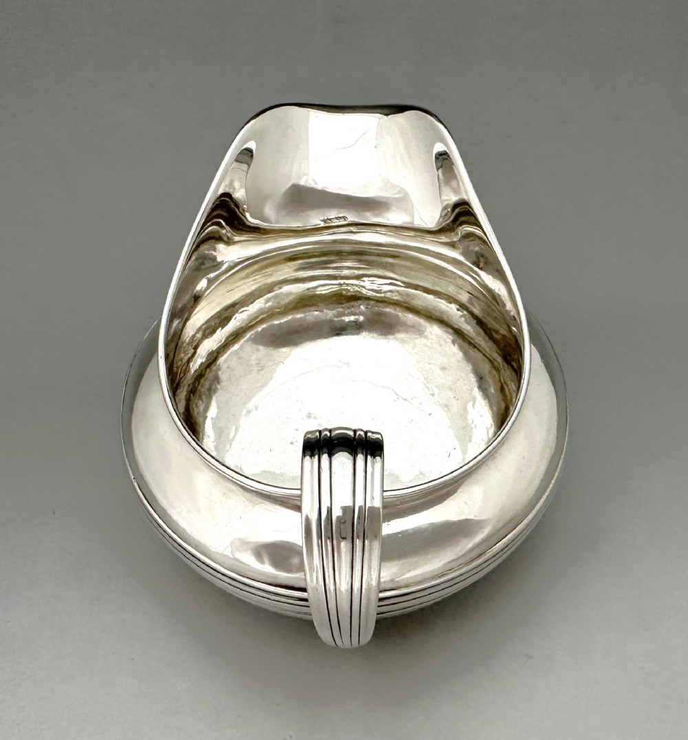 A George IV sterling silver cream jug with a polished surface, horizontal reeded decoration on the waist, a wide pour spout, and a curved high-loop handle. View VII