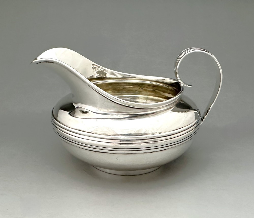 A George IV sterling silver cream jug with a polished surface, horizontal reeded decoration on the waist, a wide pour spout, and a curved high-loop handle. View VIII