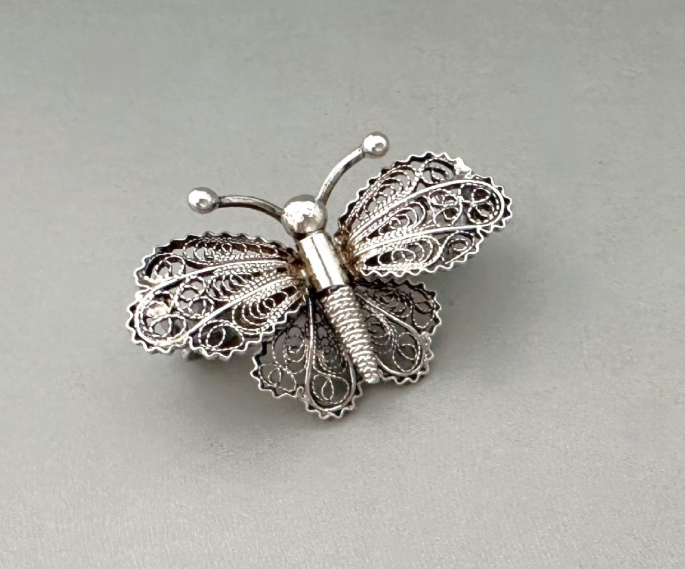 A sterling silver filigree brooch shaped like a butterfly with detailed openwork lace wings, textured body, and ball-tipped antennae.