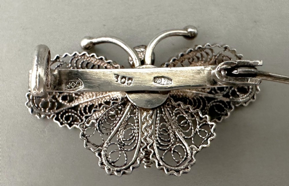 A sterling silver filigree brooch shaped like a butterfly with detailed openwork lace wings, textured body, and ball-tipped antennae. View IV