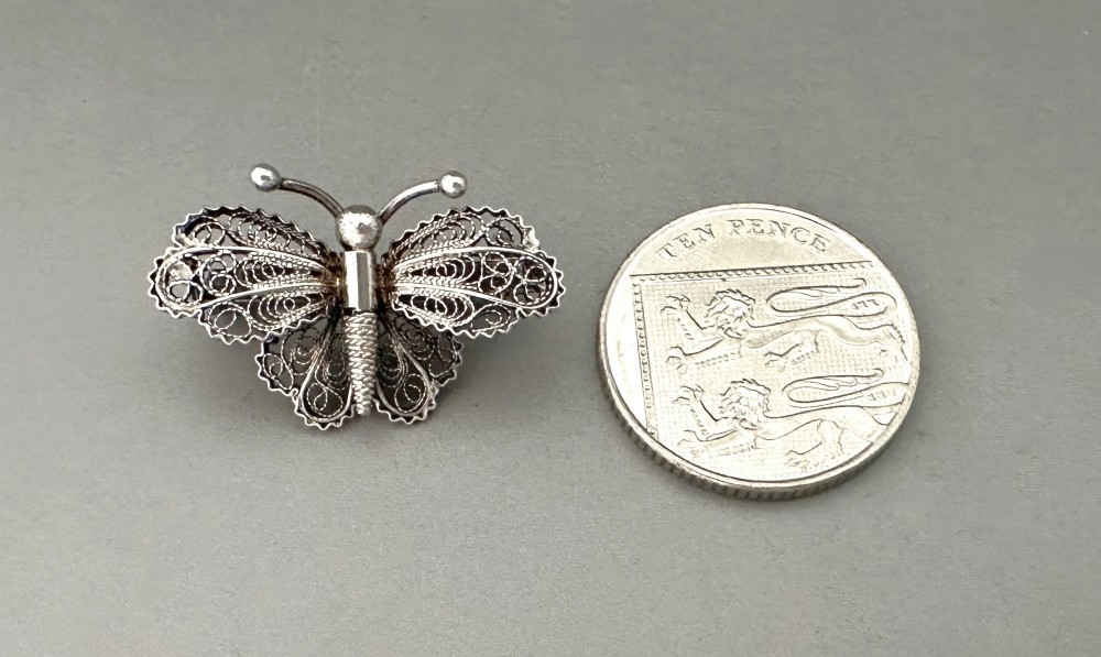 A sterling silver filigree brooch shaped like a butterfly with detailed openwork lace wings, textured body, and ball-tipped antennae. View V