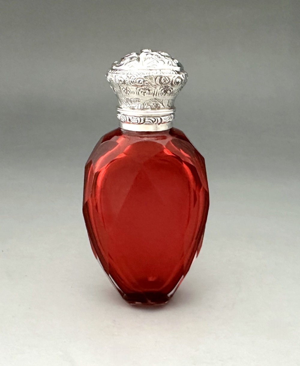 A Victorian faceted ruby red glass scent bottle featuring an intricately embossed silver cap.