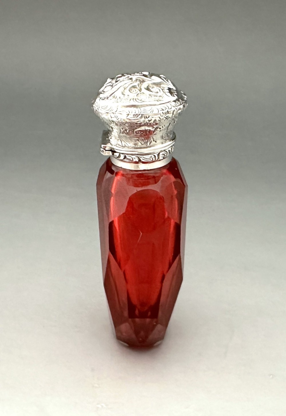 A Victorian faceted ruby red glass scent bottle featuring an intricately embossed silver cap. View III