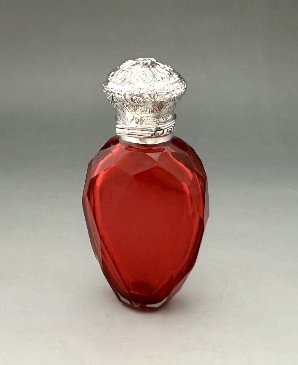 A Victorian faceted ruby red glass scent bottle featuring an intricately embossed silver cap. View IV