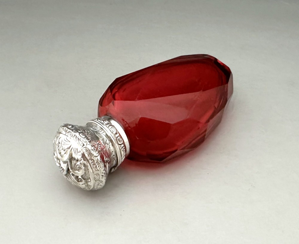A Victorian faceted ruby red glass scent bottle featuring an intricately embossed silver cap. View V