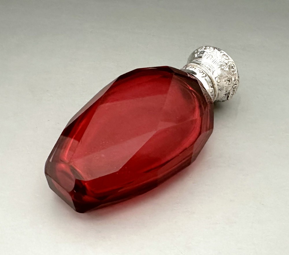 A Victorian faceted ruby red glass scent bottle featuring an intricately embossed silver cap. View VI