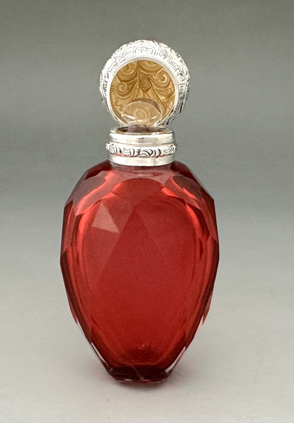 A Victorian faceted ruby red glass scent bottle featuring an intricately embossed silver cap. View VII