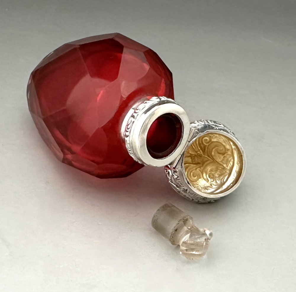 A Victorian faceted ruby red glass scent bottle featuring an intricately embossed silver cap. View VIII