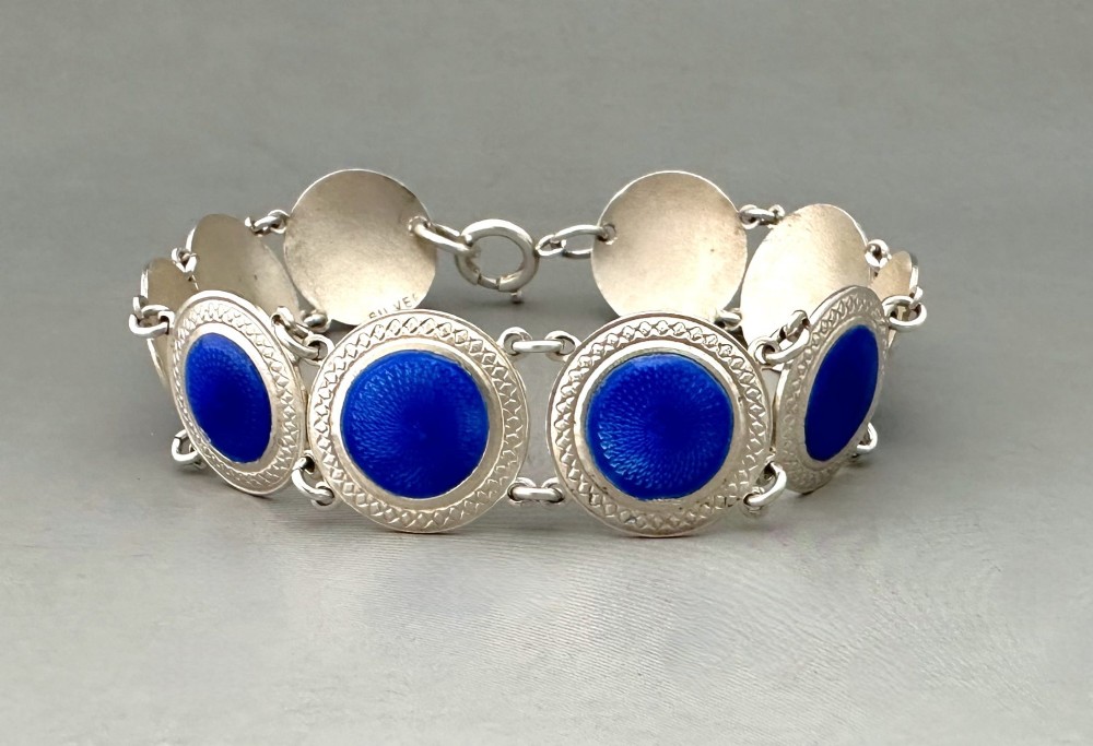 An Art Deco silver link bracelet featuring circular panels filled with cobalt blue guilloche enamel.