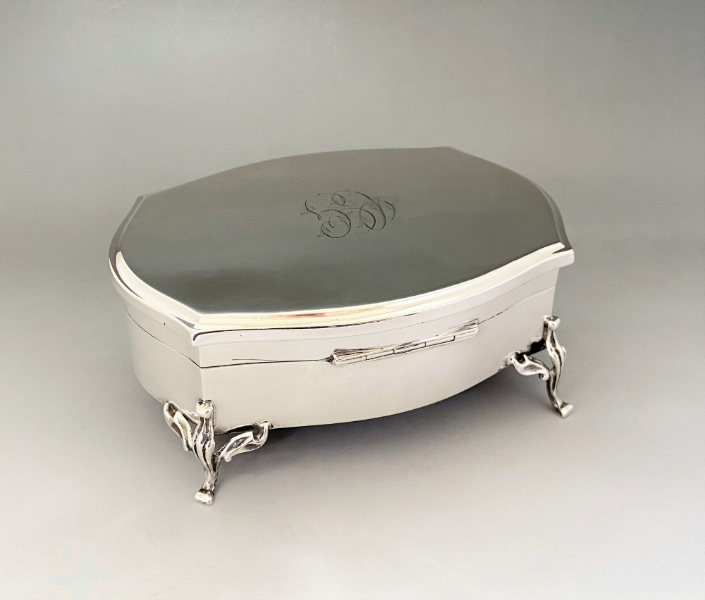 A silver jewellery trinket box with a hinged monogrammed lid supported on four decorative cabriole legs.