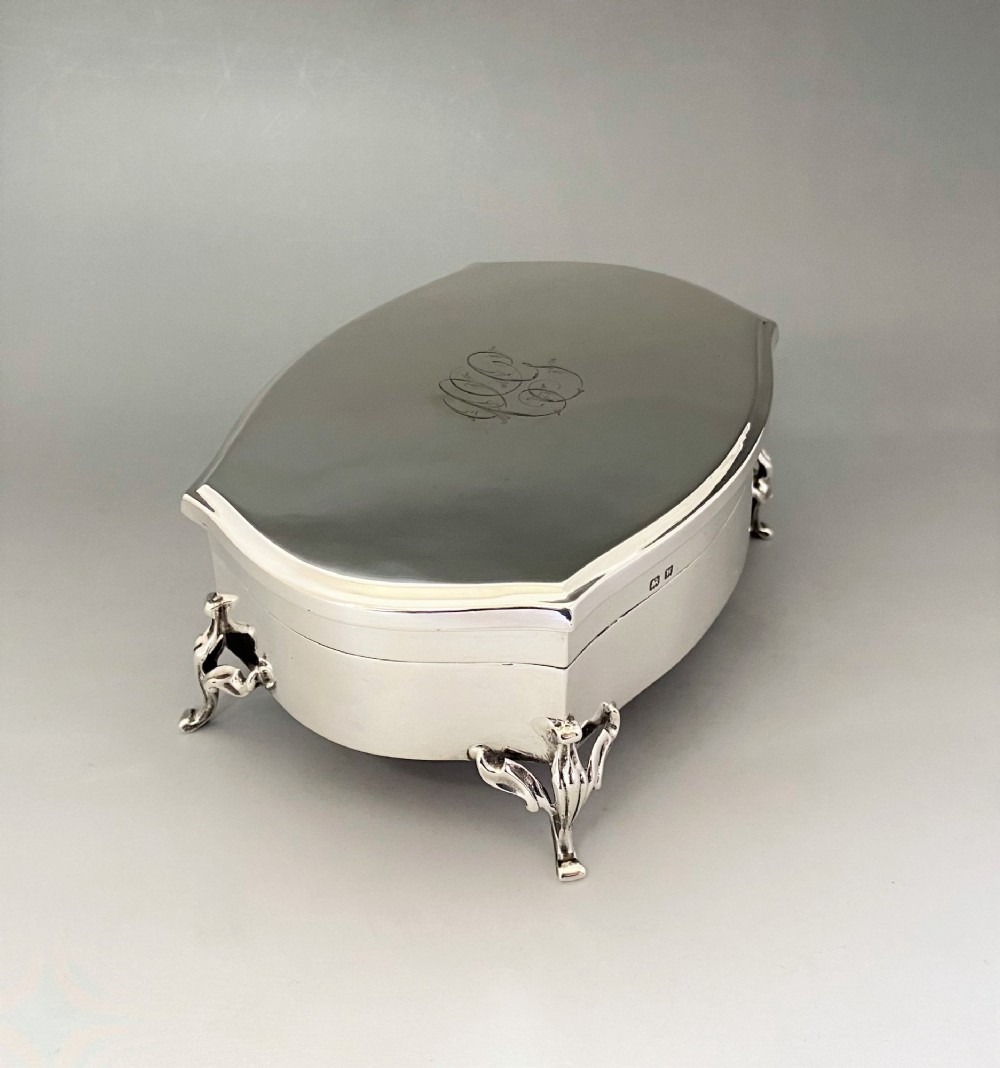 A silver jewellery trinket box with a hinged monogrammed lid supported on four decorative cabriole legs. View IV
