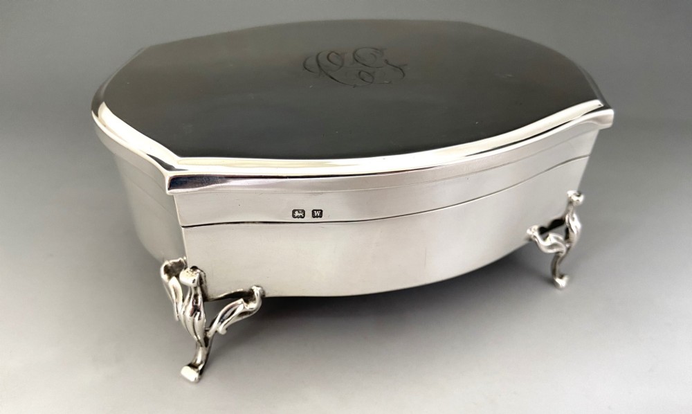 A silver jewellery trinket box with a hinged monogrammed lid supported on four decorative cabriole legs. View X