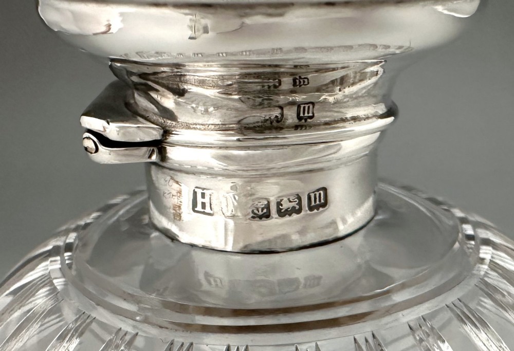 A globular clear fluted glass cologne bottle featuring a silver collar and an engine-turned circular top. View VI