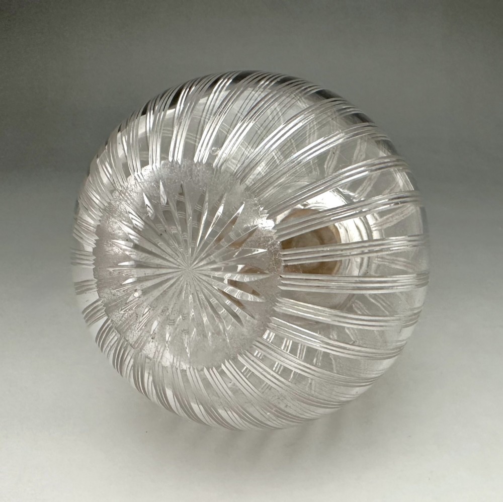 A globular clear fluted glass cologne bottle featuring a silver collar and an engine-turned circular top. View VII