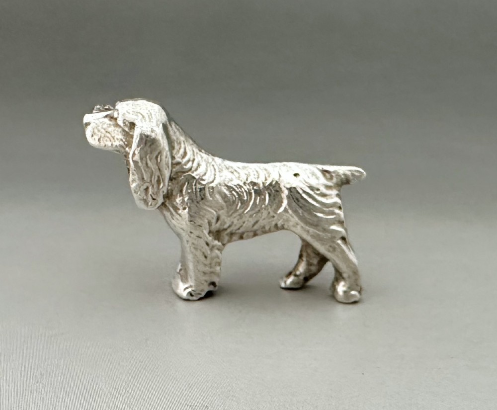 A cast silver brooch finely detailed in the shape of a standing spaniel dog with textured fur.
