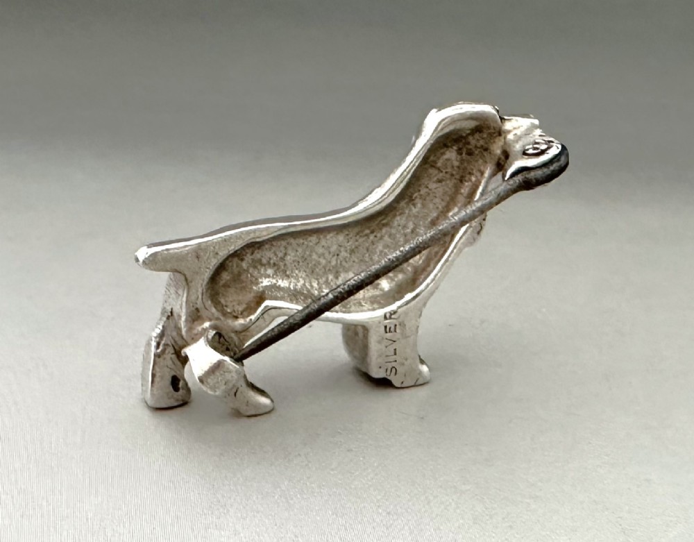 A cast silver brooch finely detailed in the shape of a standing spaniel dog with textured fur. View III