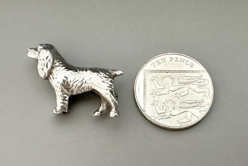 A cast silver brooch finely detailed in the shape of a standing spaniel dog with textured fur. View VI