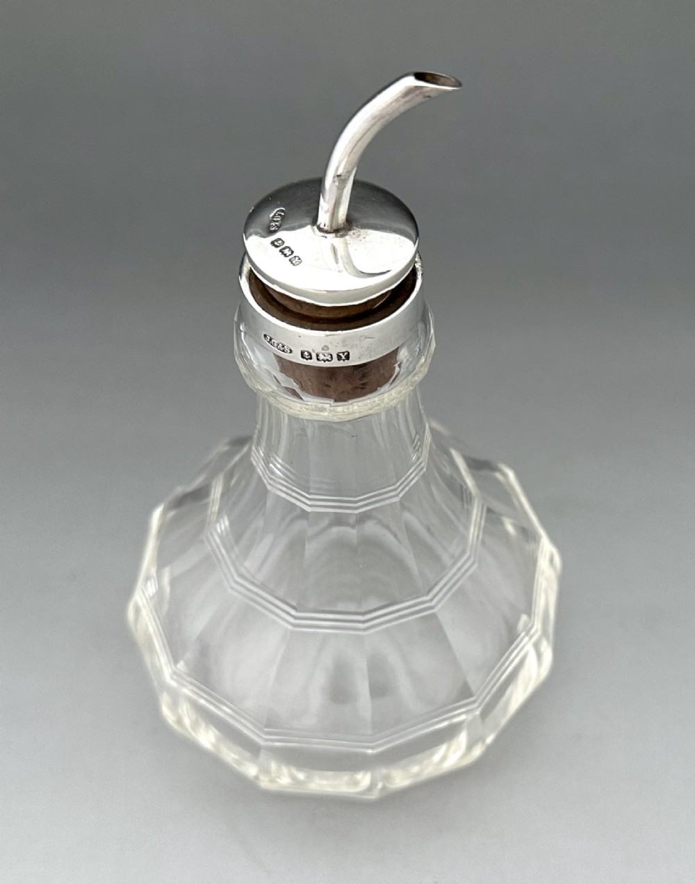 An Art Deco clear faceted glass bitters bottle featuring a hallmarked silver collar and curved pouring spout stopper. View II