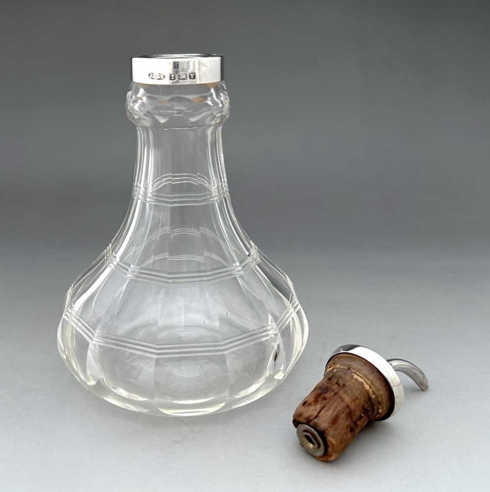 An Art Deco clear faceted glass bitters bottle featuring a hallmarked silver collar and curved pouring spout stopper. View V