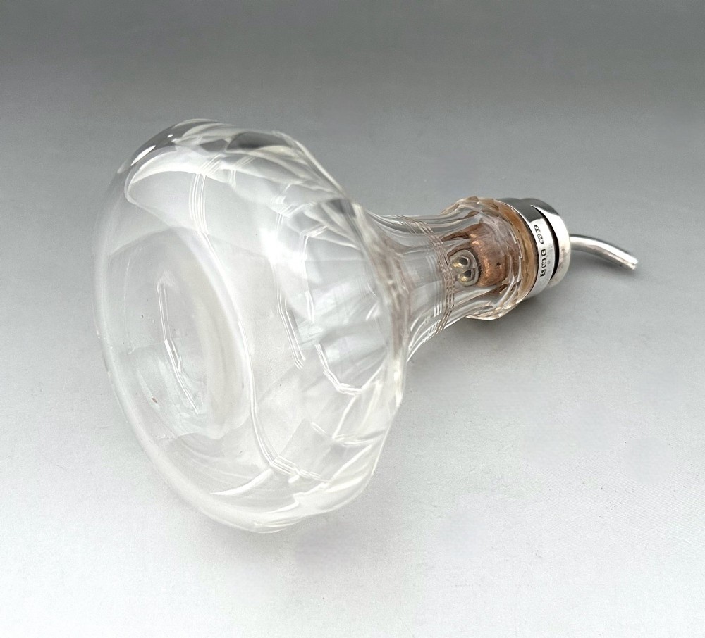 An Art Deco clear faceted glass bitters bottle featuring a hallmarked silver collar and curved pouring spout stopper. View VI